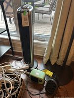 Photo of the three items: Bionaire tower fan, small green heater, small black Honeywell heater on floor near window