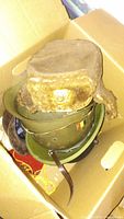 Photo of box containing vintage military hats and helmets, showing stacked helmets and a fur Soviet winter hat with emblem.