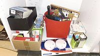 Assorted household items including tools and batteries in red container, boxes of light bulbs and faucet visible.