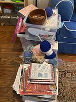 Full lot view showing clear plastic containers filled with yarn, knitting tools, a large stack of knitting books and patterns, plus yarn skeins and a yarn winder on top.