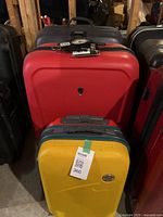 Front view of three stacked suitcases: yellow Eminent at front, red Heys in middle, black Samsonite in back, with luggage scale and tag on top.