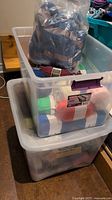 Two clear plastic totes filled with multiple skeins of yarn in assorted colors and types, stored in plastic bags within totes.