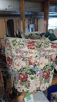 Photo showing the floral fabric bag filled with assorted needle crafting supplies including cross stitch fabric and needles.