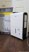 Front view of Omni Max 50 pint dehumidifier with original box, showing clean white body and black side panel.