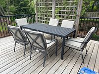 Overview of black patio table and six matching arm chairs on wooden deck