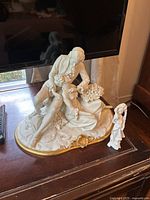 Large porcelain Capodimonte couple sculpture displayed on wooden surface with TV in background