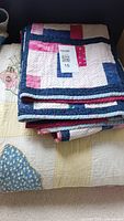 Folded geometric patchwork quilt in pink, red, blue, and white on top of a quilt with butterfly appliqués