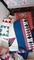 Four quilts stacked, showing various patchwork and star designs with red, white, blue, and black colors.
