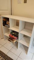 Front view of white melamine 3x3 cubby shelf unit with some items inside some cubbies.