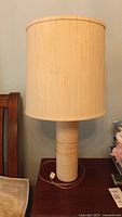 Full view of the vintage table lamp showing its tall cylindrical heavy base and beige cloth lampshade.