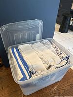 Plastic tote full of various folded table linens with visible patterns and stripes in blue and white.
