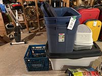Stacked blue Rubbermaid Roughneck storage tubs with black lids, small clear plastic bin on top, blue crate to the side, and two white step stools visible.