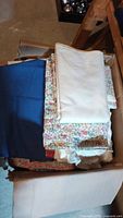 Box containing folded vintage fabric pieces including floral prints, solid colors, and multiple textures.