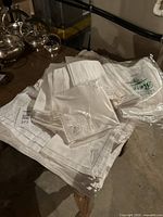 Pile of vintage white table linens including placemats and napkins with some silverware on table corner.