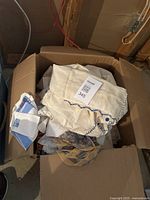 Box of assorted vintage linens mostly cream color with some blue embroidery and lace trim visible