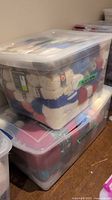 Large clear plastic tote filled with variegated yarn in multiple colors including white, red, blue, and more, stacked on another tote