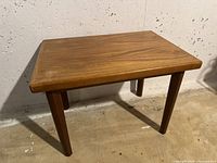 Overall angled view of the small rectangular wooden footstool with four legs in natural wood finish.