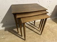 Set of three wooden nesting tables stacked together showing tapered legs and rustic brown finish