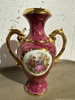 Side view of the vintage pink porcelain vase featuring the classical couple illustration, ornate gold handles and gold rim accents.