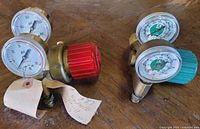 Two brass air pressure gauges on wooden surface, showing PSI dials and adjustment knobs with tags.