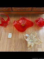 Four handmade glass bowls on wood floor: three orange Murano style and one clear Chalet style with gold flecks