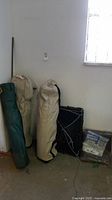 Four camping items including one green folding camp chair in storage bag with visible Team Gear tag, two beige camp beds in carrying cases, and a tarpaulin in package.