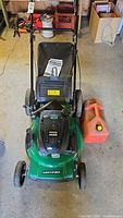 Front angled view of the green Certified lawn mower with grass catcher, engine cover and jerry can placed on the right side