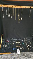 Full view of assorted necklaces hanging, and bracelets, earrings, brooches arranged below on black fabric