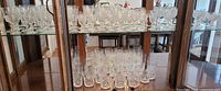 Wide view of cut crystal glasses and stemware set displayed inside a wooden cabinet with glass shelves.