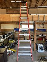Full front view of an orange-red fibreglass step ladder with 10 ft height, placed in a workshop setting showing overall condition and construction.