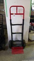 Front view of wheeled hand dolly with red and black metal frame and solid tires