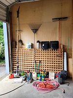 Overall view of lot contents including lattice panels, wood posts, garden tools, trimmer head, manual, extension cord and supplies