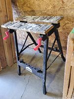 Front angle view showing two workbench frames side by side with metal legs, red clamping handles, and worn wooden tops removed.