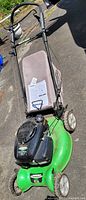Full view of green Lawn-Boy lawn mower with tan rear grass collection bag, black handle, and engine on concrete surface.