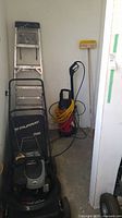 Photo showing the Murray gas lawn mower, Husky pressure washer, and aluminum stepladder together against a wall.