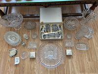 Overview of glass and crystal bowls, trays, and other items arranged on wooden floor.
