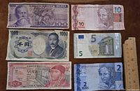 Six paper banknotes arranged with a ruler for scale, displaying Mexican 100 and 20 peso notes, Japanese 1000 yen note, Brazilian 10 and 2 reais notes, and a 5 euro note.