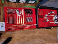Top down view showing two open cases containing the full flatware set with forks, knives, spoons, and serving pieces organized in red fabric liners.