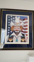 Framed clown print wearing cowboy hat and bolo tie in front of an American flag.