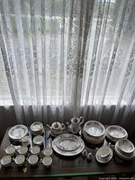 Full spread of tea service, dinnerware and serving pieces on table under lace curtains