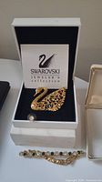 Gold-tone swan brooch in box with Swarovski Jeweler's Collection branding and accompanying gold-tone bracelet with crystal rhinestones.