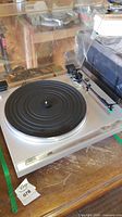 JVC silver turntable with clear dust cover, tonearm, and rubber platter mat on wooden table.