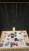 Wide shot of multiple pairs of earrings laid out and some necklaces hanging above them
