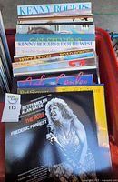 Photo showing stack of vinyl records including artists Kenny Rogers, Cat Stevens, Bette Midler, Alan Bates, and Frederic Forrest with colorful album covers.