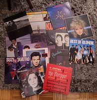 Photo showing multiple vinyl LP albums arranged on a carpet, featuring artists such as Blondie, Suzi Quatro, and Rick Astley.