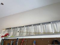 Full view of the aluminum extension ladder hanging horizontally above a workbench in a garage area.
