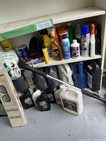 Two shelves of automotive fluid containers and bottles with a black and silver telescoping handle tool leaning in front.