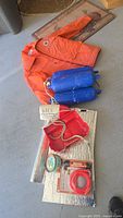 Photo showing Mustang orange floater jacket, blue pump, and boating accessories including tube, bucket, can, and rope.