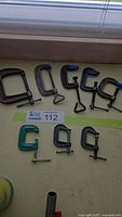 Eight steel C-clamps of varying sizes and colors, arranged on a surface under a window, showing overall lot contents
