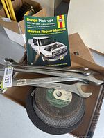 Photo showing the Haynes Dodge Pick-ups repair manual, several combo wrenches, and stacked sanding discs underneath.